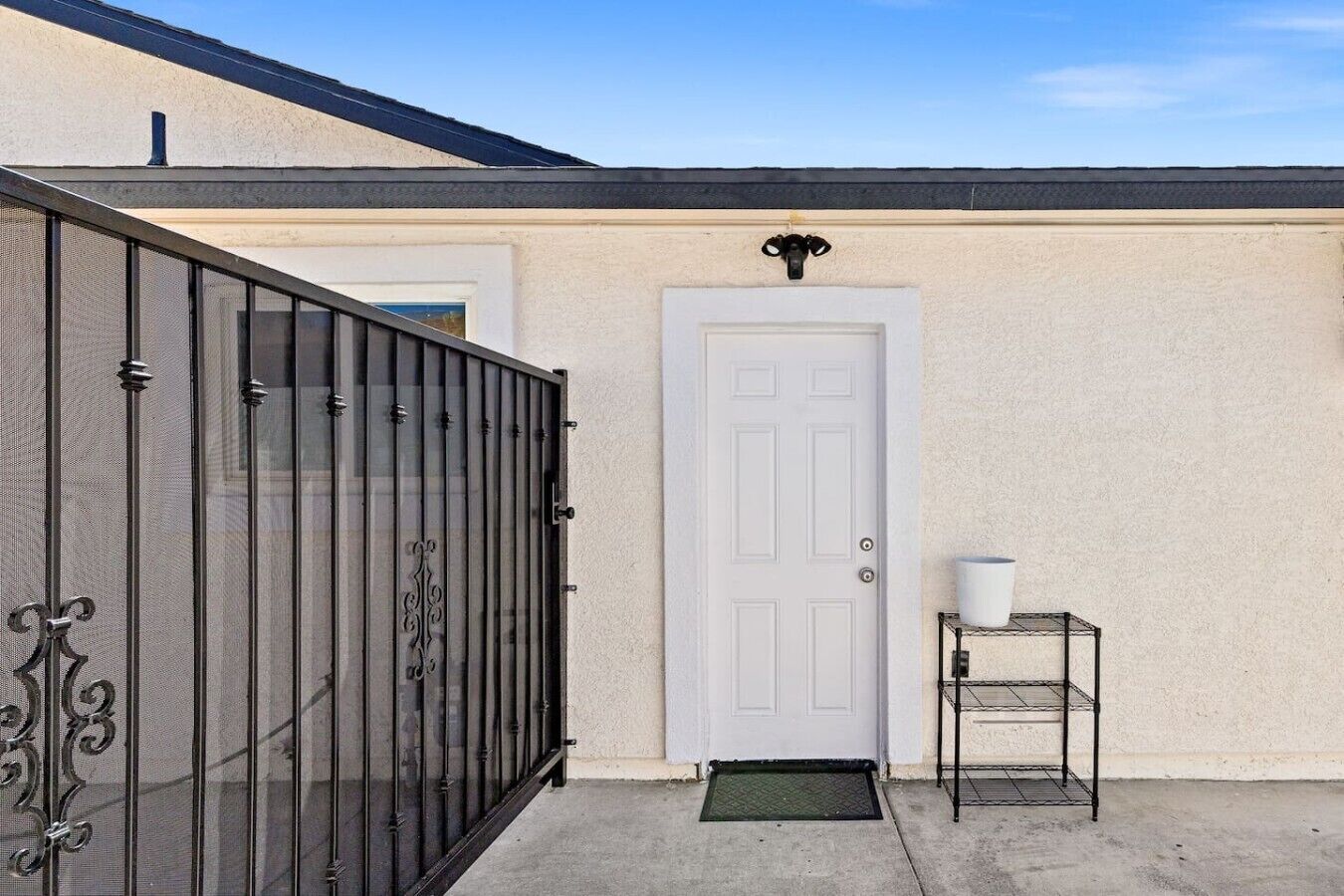 A house with a white door, a black metal gate, and a small metal shelf with a white container.