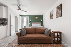 A bedroom with a bed, a brown sofa, a small wooden table, and a ceiling fan. - Brighthill Haven | Cozy Studio | 10 Min to Strip (Las Vegas)