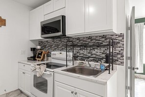 A modern kitchen with white cabinetry, a black microwave, a coffee machine, a sink, and a tiled backsplash. - Brighthill Haven | Cozy Studio | 10 Min to Strip (Las Vegas)
