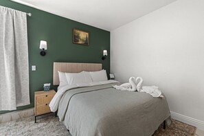 Un lit bien fait, avec une tête de lit, une table de chevet sur laquelle se trouve une lampe, et un tableau accroché au mur.