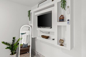 A modern living room with a mounted TV, white shelves, a mirror, and a plant. - Brighthill Haven | Cozy Studio | 10 Min to Strip (Las Vegas)