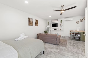 A bedroom with a bed, a sofa, a ceiling fan, a TV, a desk, and a small kitchenette. - Brighthill Haven | Cozy Studio | 10 Min to Strip (Las Vegas)