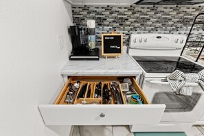 A kitchen with a marble countertop, a coffee maker, a sign reading 'WELCOME FAMILY', and a drawer with utensils. - Brighthill Haven | Cozy Studio | 10 Min to Strip (Las Vegas)