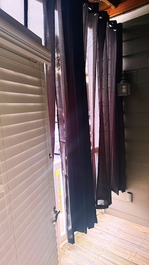 Ein Zimmer mit Holzboden, einem Fenster mit Jalousien und einer Vorhangstange mit mehreren Vorhängen.