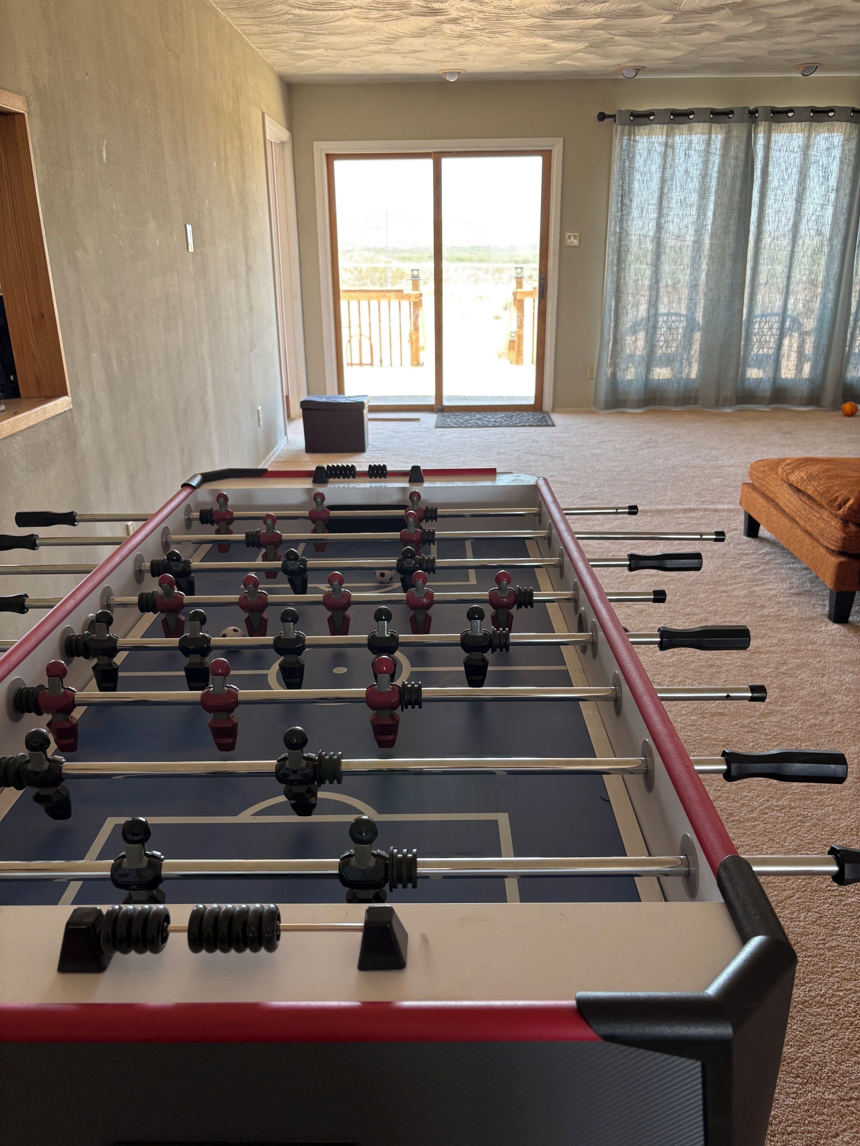 Une table de baby-foot dans une pièce dotée d’une grande fenêtre, d’une porte et d’un canapé.