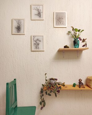 Ein Zimmer mit einem grünen Stuhl, einem hölzernen Regal mit einer Pflanze und gerahmten Kunstwerken an der Wand.