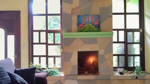 A living room with a stone fireplace, a sofa, and a blue rug. - •Blood and Wisdom • Home - Art Gallery • Lodging, art, clay, and cardboard crafts• (San Cristóbal de las Casas)