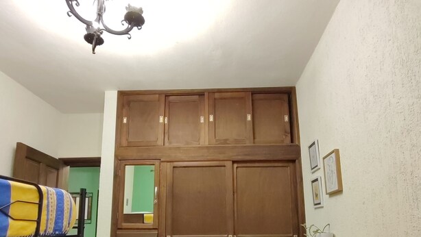 A bedroom with a bunk bed, a wardrobe with multiple compartments, a small shelf with decorative items, and a wall clock. - •Blood and Wisdom • Home - Art Gallery • Lodging, art, clay, and cardboard crafts• (San Cristóbal de las Casas)
