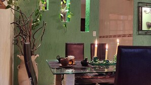 A dining area with a glass table, chairs, a vase with branches, and a candle.