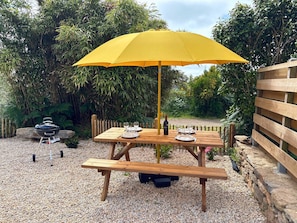 An outdoor dining area with a wooden table and bench, a yellow umbrella, and a barbecue grill. - Peskaour, An artist s house near the sea (Landéda)