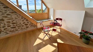 Un dormitorio tipo loft con techo inclinado, una escalera de madera, una pequeña mesa con sillas y vistas al cielo y al paisaje.