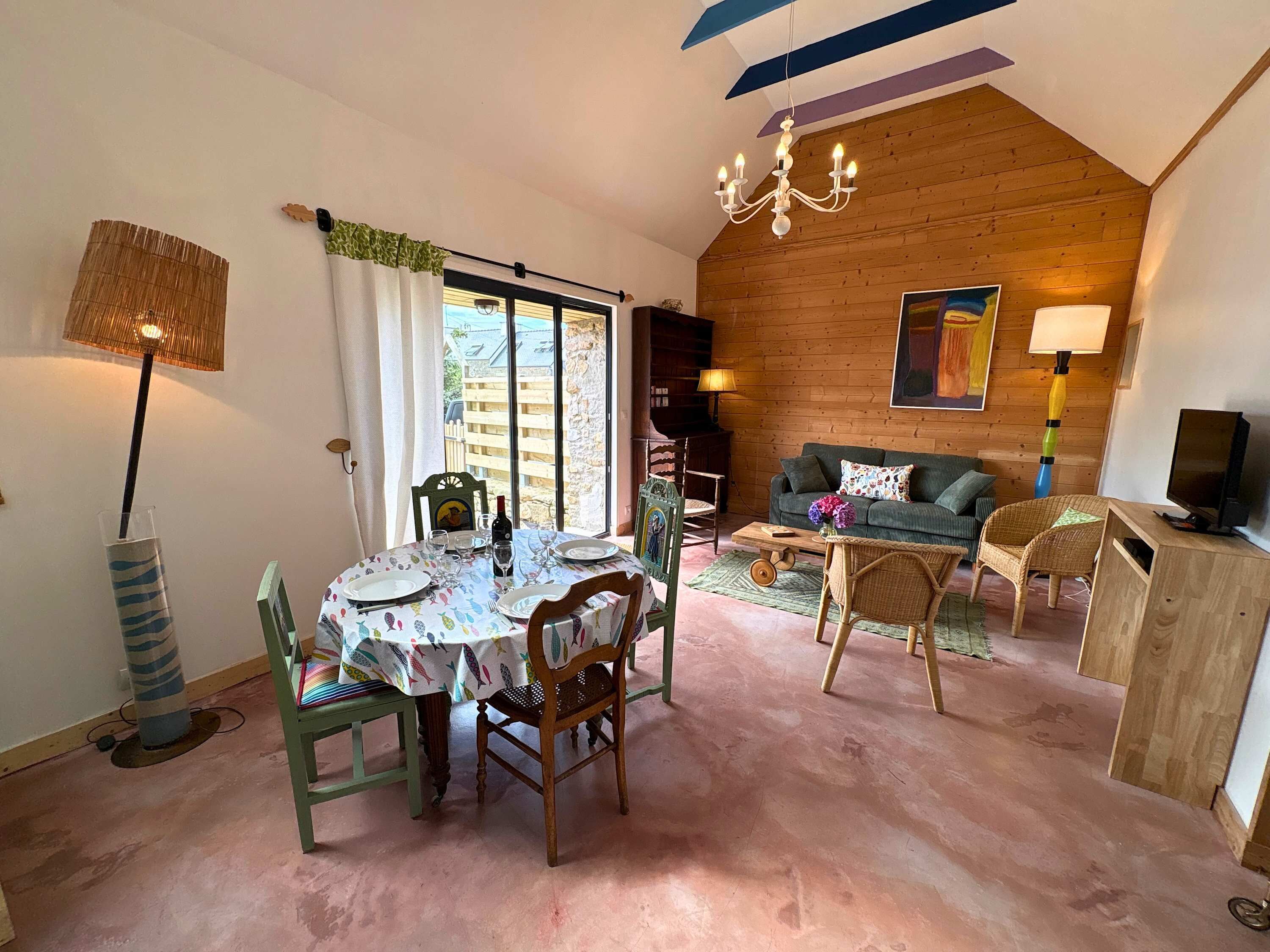Une pièce chaleureuse avec une table à manger dressée pour deux personnes, un canapé, un téléviseur et un lustre.