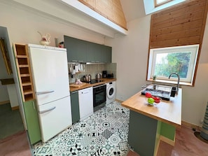 A compact kitchen with a built-in washing machine, a wooden countertop, and a window with a view of greenery. - Peskaour, An artist s house near the sea (Landéda)