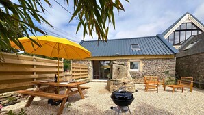Un patio con mesa de madera, un paraguas amarillo, una parrilla y paredes de piedra.