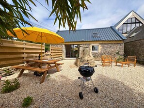 Eine Terrasse mit Holztisch, gelbem Sonnenschirm, Grill und Steinmauern.