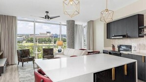 A modern kitchen with a large island, dark cabinetry, and a view of a building through large windows.