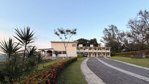 A multi-story building with a central courtyard, surrounded by manicured gardens and a paved driveway.
