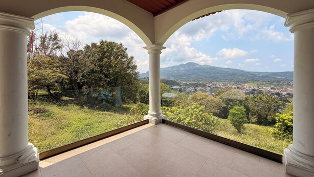 Un balcón cubierto con columnas blancas y vistas a la ciudad y montañas.