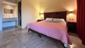 Habitación de hotel con cama, baño con espejo y lavamanos, y dos luces fijadas a la pared.