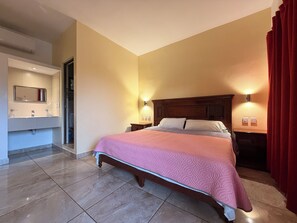 Hotelkamer met een bed, een badkamer met spiegel en wastafel, en twee wandlampen.