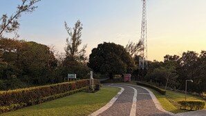Un camino empedrado que lleva a la entrada de un hotel, con un letrero, rodeado de setos y árboles bien cuidados.