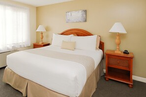 A hotel room with a large bed, two bedside tables with lamps, a window with blinds, and a wall-mounted artwork.