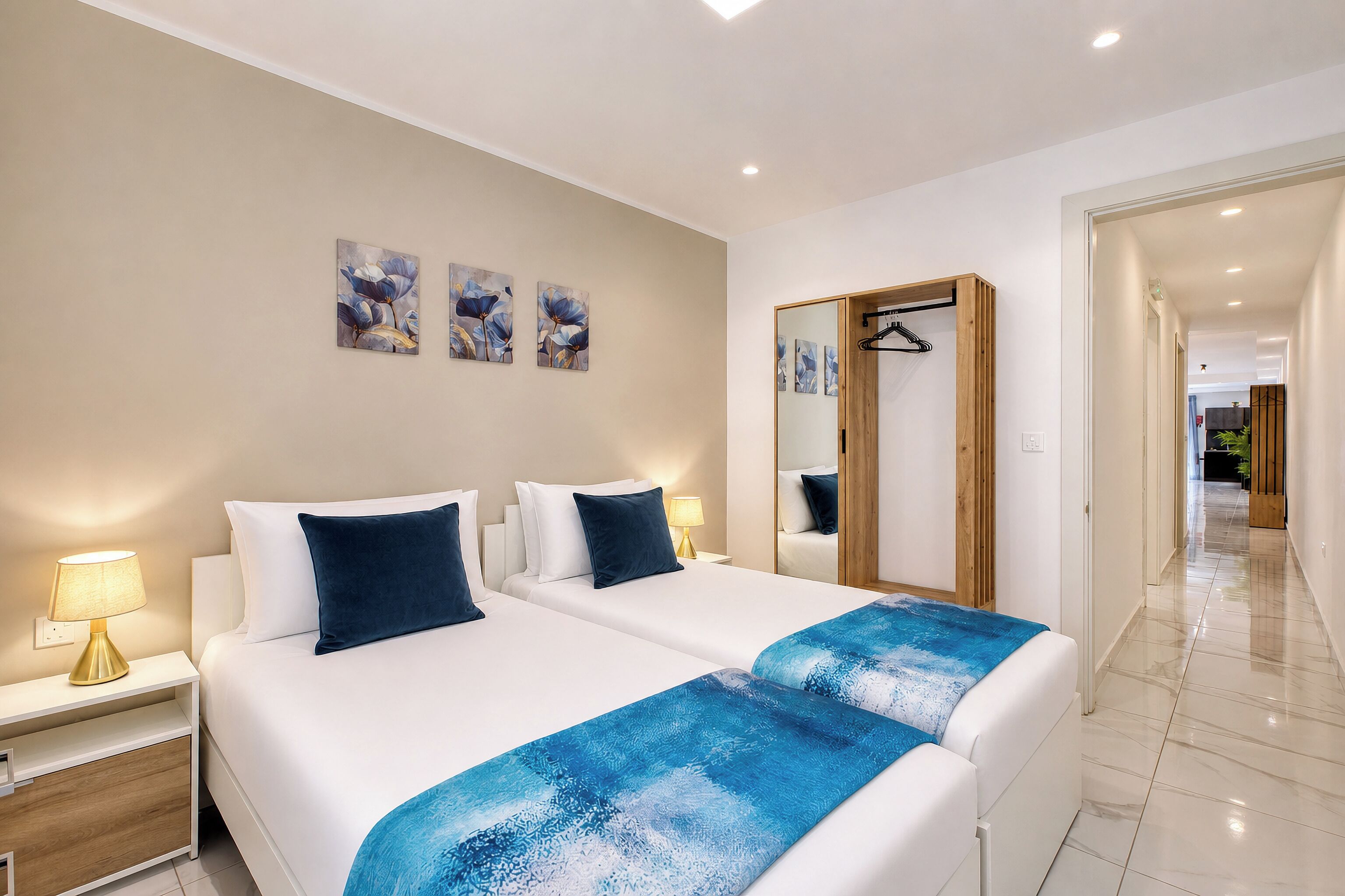 Habitación de hotel con dos camas, una mesita de noche con lámpara, un espejo y una obra de arte en la pared.