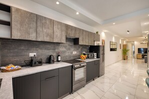 A modern kitchen with a built-in oven, microwave, and a large island with a bowl of fruit. - Urban Haven - Stylish 2BR Apartment with Lift & Balconies (Il-Gżira)