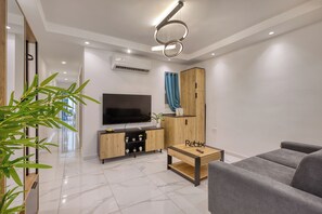 A modern living room with a flat-screen TV, wooden furniture, a grey sofa, and a small table with a remote. - Urban Haven - Stylish 2BR Apartment with Lift & Balconies (Il-Gżira)