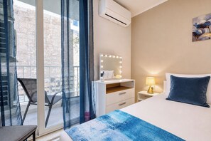 Ein Hotelzimmer mit Bett, Nachttisch mit Lampe, Schminktisch mit Spiegel und Balkon mit Stuhl.