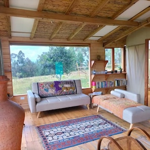 A wooden cabin interior with a sofa, a patterned rug, and a bookshelf. - Espectacular Casa Yurta (Villa de Leyva)