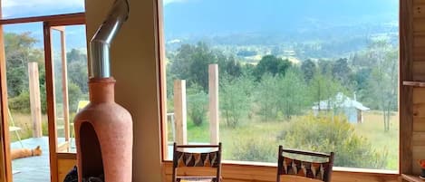 Ein rustikales Interieur mit großem Kamin, Holzmöbeln und Blick auf eine grüne Landschaft.