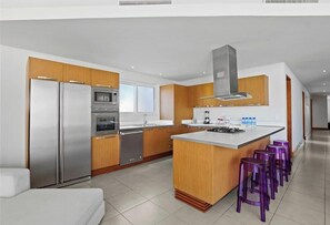 Una cocina moderna con electrodomésticos de acero inoxidable, armarios de madera, una isla central con taburetes y un amplio ventanal.
