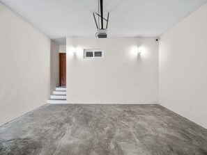 Una habitación con piso de concreto, paredes blancas, un ventilador de techo y una escalera que conduce a otra zona.