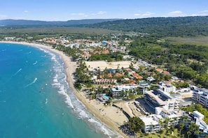 Vista aérea de un pueblo costero con propiedades frente al mar, una playa y vegetación circundante.