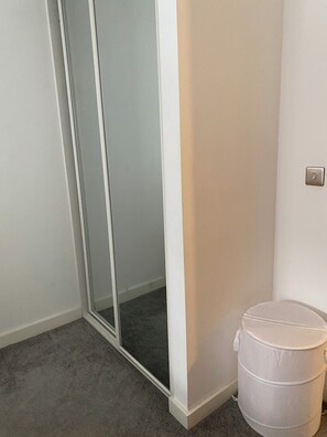 Ein Zimmer mit einer Schiebetür aus Glas, einer weißen Wand, einem Lichtschalter und einer weißen Mülltonne.
