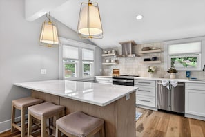 A modern kitchen with a large island, pendant lights, and a view of the outdoors. - Grand Louisville estate near Historic Churchill! (Louisville)