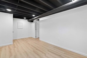 A room with white walls, a wooden floor, a door, and a ceiling with exposed pipes. - Grand Louisville estate near Historic Churchill! (Louisville)