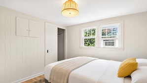 Ein Schlafzimmer mit einem Bett, einem Fenster, einer Tür und einer Pendelleuchte.