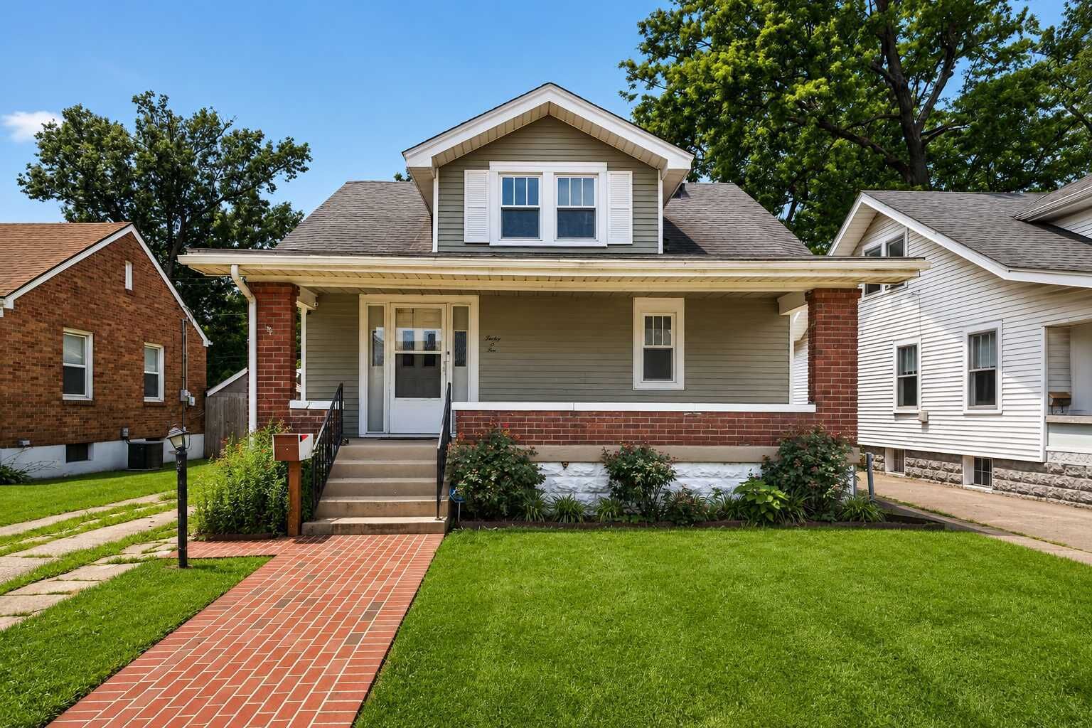 A two-story house with a front porch, a brick foundation, and a well-maintained lawn.
