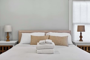 A neatly made bed with white linens, a headboard with a tufted design, and two bedside lamps on wooden nightstands. - Grand Louisville estate near Historic Churchill! (Louisville)