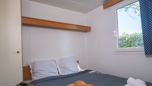 A bedroom with a bed, pillows, a window, and a hat on the bed. - Camping City (Arles)