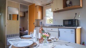 A compact kitchen with a microwave, a small refrigerator, and a dining area set with plates, glasses, and a vase of flowers. - Camping City (Arles)