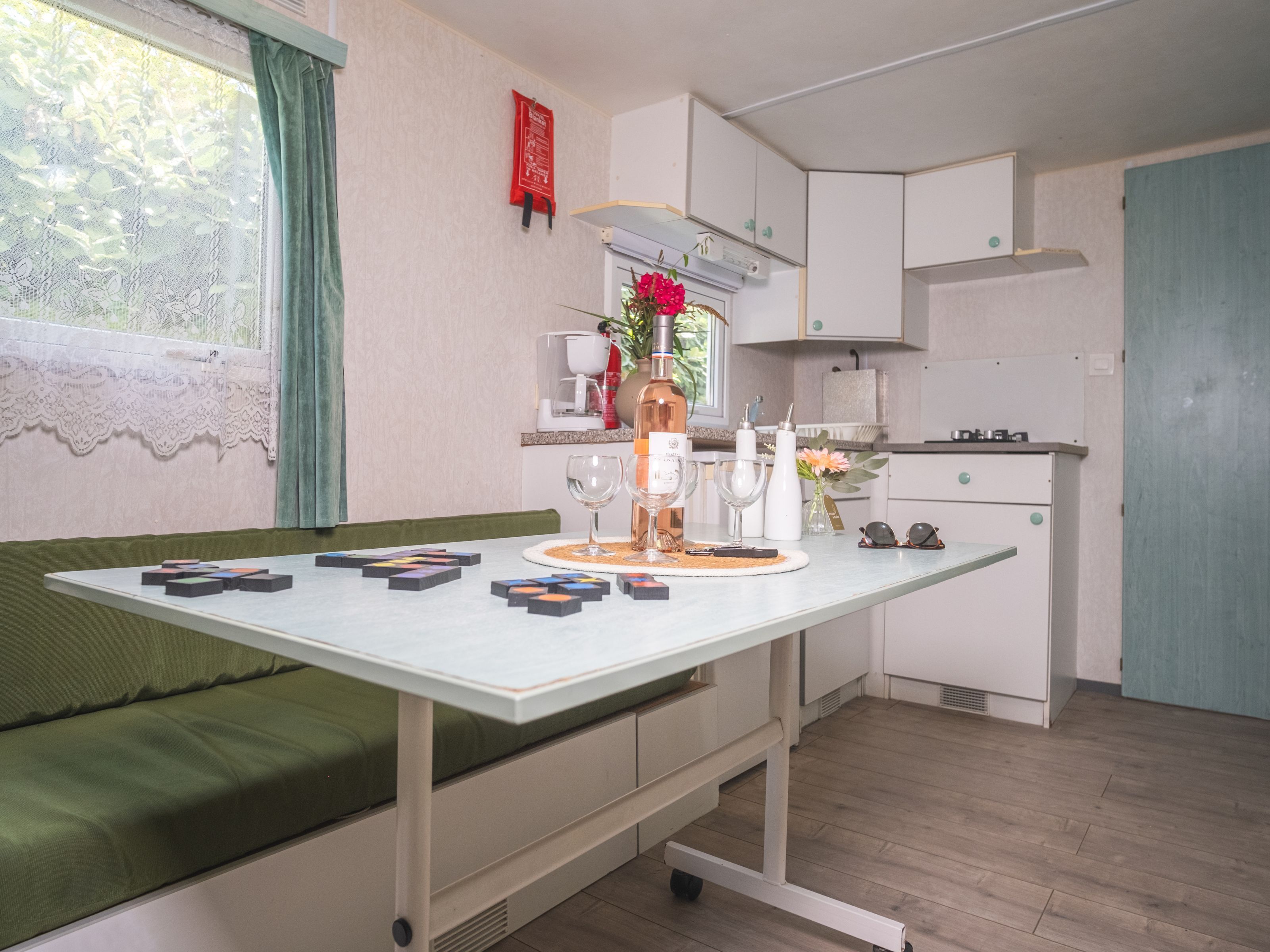 A compact kitchen with a dining table, a sofa, and a small window with lace curtains.