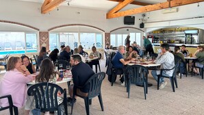 A restaurant with outdoor seating, wooden beams, and a view of the sea. - Camping City (Arles)