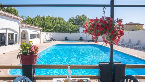 A poolside view with a table set for breakfast, a hanging flower arrangement, and lounge chairs. - Camping City (Arles)