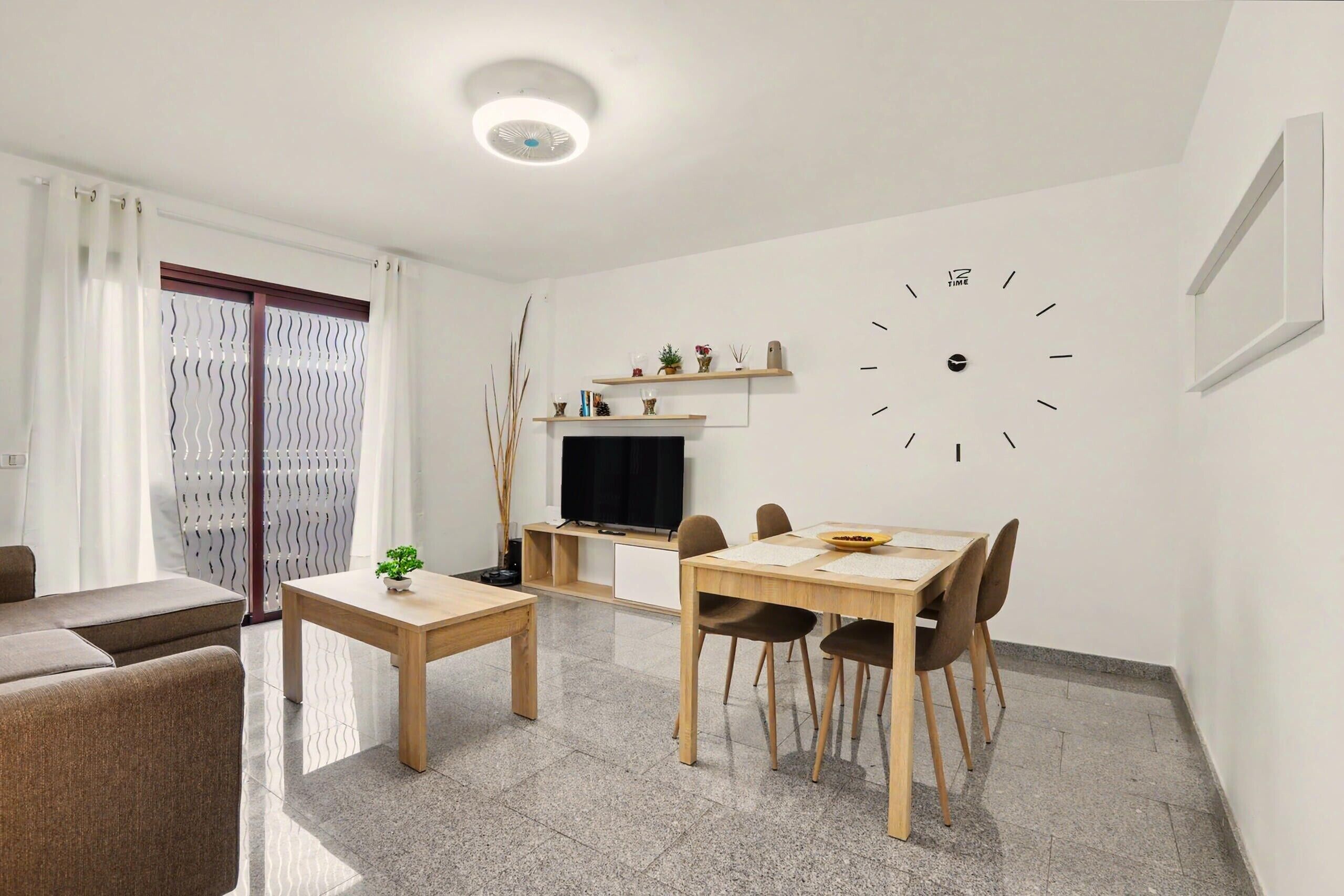 Een moderne woonkamer met een bank, een eettafel met stoelen, een televisie en een wandklok.