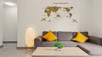 Un interior moderno con un mapa mundial en la pared, un sofá gris con cojines amarillos, una mesa de centro de madera y una pequeña planta en maceta.