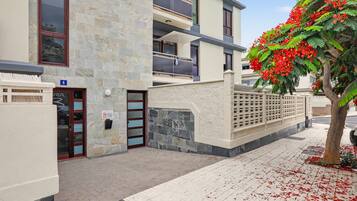 Un edificio de varios pisos con fachada de piedra, una entrada con portón y un árbol con flores rojas.