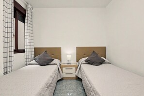 Habitació doble amb dos llits, una nitòria amb una làmpada i una finestra amb cortines estampades.